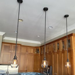 3 new pendant lights - Three pendant lights with glass shades are suspended from the ceiling in a kitchen with wooden cabinets and stainless steel appliances.