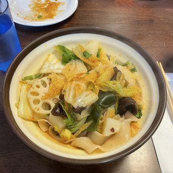 Wild Ginger - H7. Mixed Veggie Hand-pulled noodle in sauce - A large bowl of mixed vegetables and hand-pulled noodles in sauce, served on a wooden table with chopsticks and empty plates nearby. - Chinese Near Me - Alameda, California
