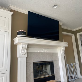 SmartHome Connect - TV installation - A large flat-screen TV is mounted above a white, ornate fireplace mantel in a living room with beige walls and crown molding. - TV Mounting Near Me