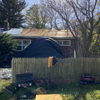 Vaz Construction - During - A backyard with a wooden fence, trees, and a house in the background, featuring construction tools and equipment on the grass. - Roofing Near Me - New Bedford, Massachusetts