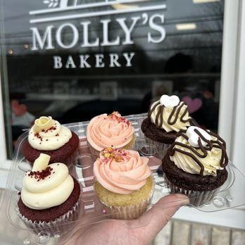 Molly's Bakery - A person holds a tray with six cupcakes featuring various frosting styles and decorations outside Molly's Bakery. - Bakeries Near Me - Beacon Falls, Connecticut