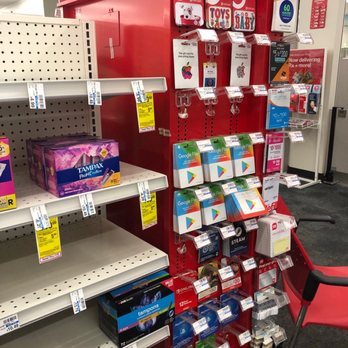 CVS Pharmacy - the shelves of the store - A Target store display with a red pegboard holding various gift cards, including Apple, Google Play, and Steam, along with phone accessories like chargers and cases. The shelves below are mostly empty, with some boxes of tampons and other personal care products. A red chair is positioned to the right of the display, and store signage is visible in the background. - Pharmacy Near Me - Ottawa, Illinois