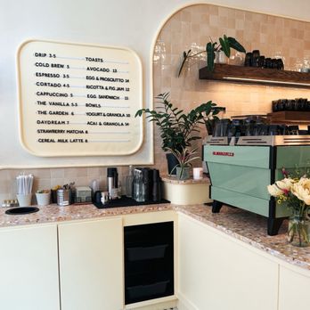 Begin - Inside - A cafe interior features a counter with a menu board, coffee machine, cups, and plants, with a tiled wall and a black-and-white patterned floor. - Coffee & Tea Near Me - Westerville, Ohio