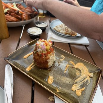 Beacon 70 Restaurant - A fried appetizer topped with diced vegetables is served on a rectangular plate at a restaurant table, with various dishes and drinks visible. - New American Near Me - Brick, New Jersey