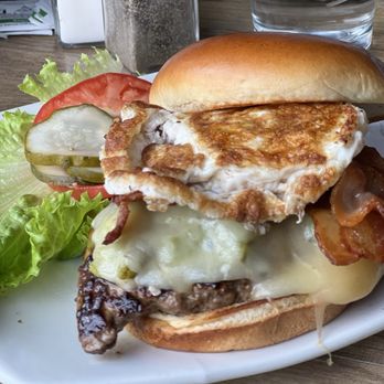 The Kosmos - Cosmic Burger with egg, bacon and green chili. - A burger featuring a fried egg, bacon, melted cheese, and beef patty on a bun, accompanied by lettuce and tomato slices, served on a white plate. - Bars Near Me - Albuquerque, New Mexico