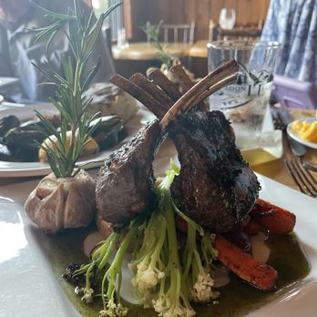 Loon Lodge - Lamb chops - perfectly cooked! - A dish with two grilled lamb chops, vegetables, and sauce is presented on a white plate, garnished with herbs. - Bed & Breakfast Near Me - Rangeley, Maine