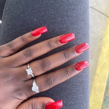 Modern Nails - A hand with red nail polish and two rings is placed on a person's lap, which is covered in dark gray fabric. - Nail Salons Near Me - Indianapolis, Indiana