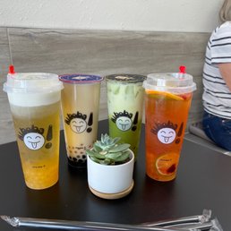 Bobas - Four bubble tea drinks with various flavors and toppings are arranged on a black table, with a small potted succulent in the center.