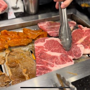 Ohgane - a person cutting meat on a grill - Korean Near Me - Concord, California Ohgane - a person cutting meat on a grill - Korean Near Me - Concord, California