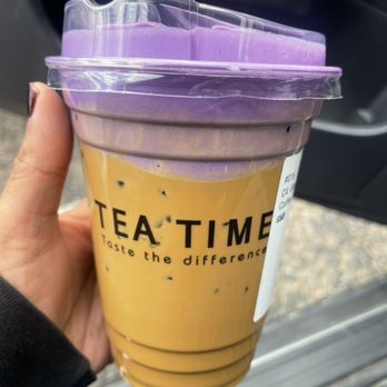 Tea Time - C4. Ube Coffee - A plastic cup of iced coffee with purple foam and a purple lid is held by a person inside a vehicle. - Coffee & Tea Near Me - Albuquerque, New Mexico