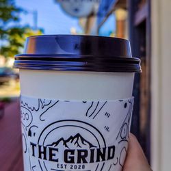The Grind - Holding a to-go cup from The Grind, with my hand in front of me, and the building sign for the coffee shop out of focus in the background