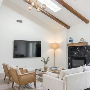 La Vie Interiors - Cozy living room retreat featuring vaulted ceilings, rustic wood beams, chic furniture, and a bold black marble fireplace. - General Contractors Near Me - San Dimas, California