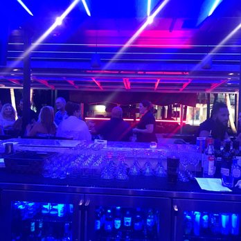 Circa69 - A bar scene with patrons seated and socializing under vibrant neon and LED lights, with a well-stocked bar and glasses on display. - Cocktail Bars Near Me - Jensen Beach, Florida