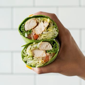 Slim Chickens - a hand holding a wrap with lettuce and tomatoes - Southern Near Me - Tallahassee, Florida