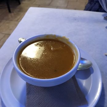 Cedar Tree - Squash was Soup of the Day - A bowl of soup with a brownish color is placed on a white plate with a spoon on the side, on a restaurant table. - Mediterranean Near Me - River Vale, New Jersey