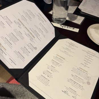Kusshi - Menu - The image shows an open menu from Kusshi Japanese restaurant on a table, with a water bottle, additional menus, and a person's hand visible. - Sushi Bars Near Me - Silver Spring, Maryland