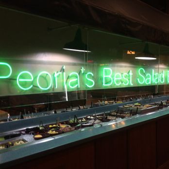 Alexander's Steakhouse - A neon sign displaying "Peoria's Best Salad Bar" in green is mounted behind a salad bar with various bowls of salad ingredients. - Steakhouses Near Me - Peoria, Illinois