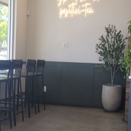 Interior - A cafe interior features a neon sign on the wall, a potted plant, and bar-height chairs along a window.