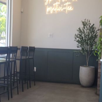 Tea Time - Interior - A cafe interior features a neon sign on the wall, a potted plant, and bar-height chairs along a window. - Coffee & Tea Near Me - Albuquerque, New Mexico