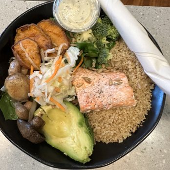 Chopsmith - A black bowl contains salmon, cooked quinoa, broccoli, avocado, mixed vegetables, and fried plantains, with a small container of dressing on the side. - Salad Near Me - Washington, DC, District of Columbia