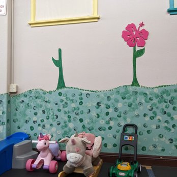 The Busy Bee - Indoor children's play area featuring toys like a unicorn ride-on, plush horse, and a toy lawnmower, with colorful wall art of trees and a flower. - Indoor Playcenter Near Me - Fallbrook, California