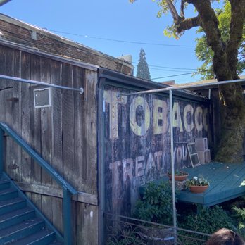 Turkey Hall - a woman sitting at a table in front of a tobacco shop - Wine Bars Near Me - Oakland, Oregon