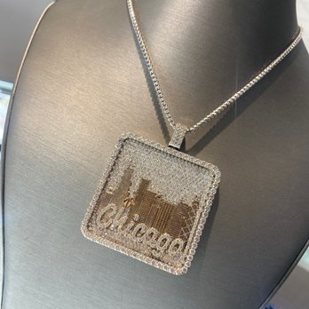 Zevar Jewelers - A silver chain necklace with a large, square pendant displaying a Chicago skyline and the word 'Chicago' is shown on a black display bust. - Jewelry Near Me - Norridge, Illinois