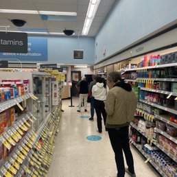 people shopping in a grocery store - Inside Walgreens in Berkeley, CA, several customers are standing in line, maintaining social distancing with markers on the floor. The store features shelves stocked with vitamins, supplements, and health products. The ceiling has fluorescent lighting, and a sign indicating pharmacy services is visible. The scene captures typical retail activity during a busy period, with customers waiting patiently at the checkout area.