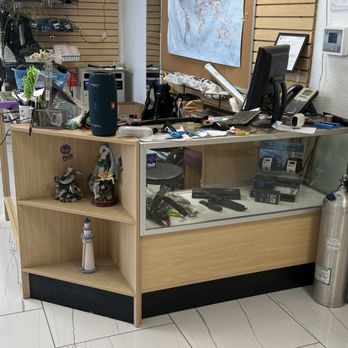 Deep Blue Scuba - A reception desk with a computer, phone, and various office supplies, surrounded by clutter and decorations. - Sporting Goods Near Me - Albuquerque, New Mexico