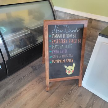 J M Global - Seasonal - A chalkboard sign lists new drinks like Mango Lemon BT, Raspberry Peach BT, and more, with a Pikachu drawing at the bottom. - Coffee & Tea Near Me - Chantilly, Virginia