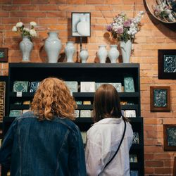 Pewabic - Two customers look at a wall of art tiles and vases.
