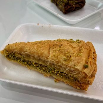 Farhat Sweets - Two Middle Eastern desserts are displayed on foam trays, one with a golden, flaky exterior topped with pistachios, and the other with a darker, layered appearance. - Desserts Near Me - Troy , Michigan