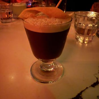 Papi - Carajillo - A dark-colored cocktail in a glass with a lemon slice garnish and a straw, set on a restaurant table with other drinks and dim lighting. - Cocktail Bars Near Me - Portland, Maine