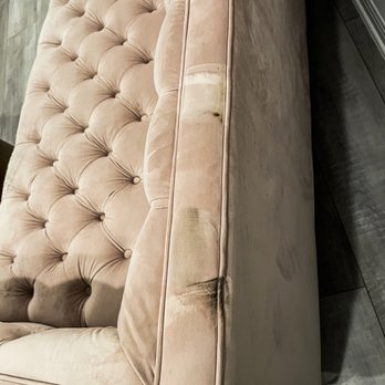 Eko Movers - A beige fabric sofa with tufted cushions is shown, with a focus on the armrest that displays visible stains, discoloration, and signs of wear. The sofa is positioned on a dark wooden floor, and the image captures the side and part of the seating area, highlighting the fabric's condition. - Movers Near Me