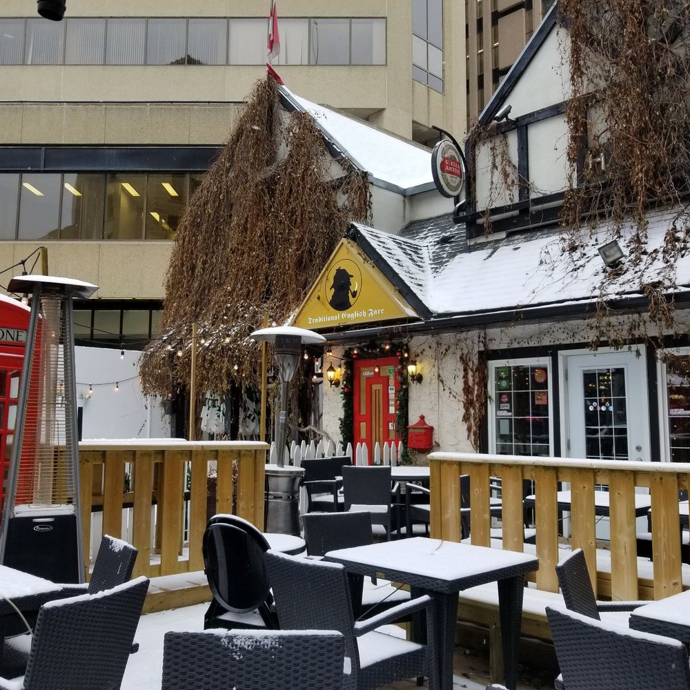 The Sherlock Holmes Pub - Cute exterior of Sherlock between the large downtown towers - Pubs Near Me - Edmonton, Alberta