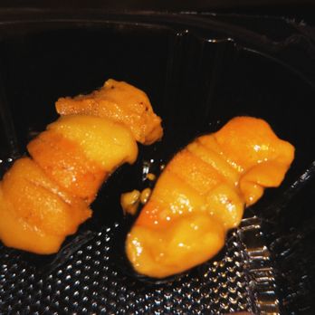 Shibui - Two pieces of sea urchin (uni) sushi are arranged in a black plastic container. The uni has a bright orange color and a smooth, creamy appearance. The container has a textured surface, and the background is dark, emphasizing the sushi pieces. - Japanese Near Me - Sunset, Florida