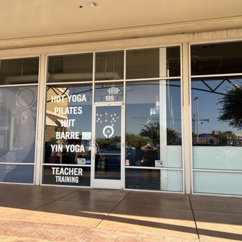The Foundry - The image shows a glass storefront of a fitness studio with white text listing classes such as hot yoga, Pilates, HIIT, Barre, Yin Yoga, and teacher training. The door has an exit sign and a small logo, with reflections of trees and buildings outside. The studio appears to be part of a family-owned chain with amenities like locker rooms and showers. - Yoga Near Me - Mesa, Arizona