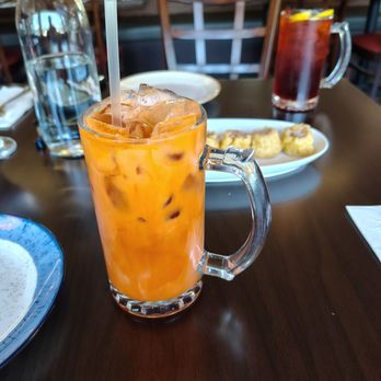 Monkey Thai Diner - Thai iced tea / small! Generous portion! - A tall glass of Thai iced tea with ice cubes and a straw is placed on a restaurant table, with other drinks and food in the background. - Thai Near Me - Clark, New Jersey