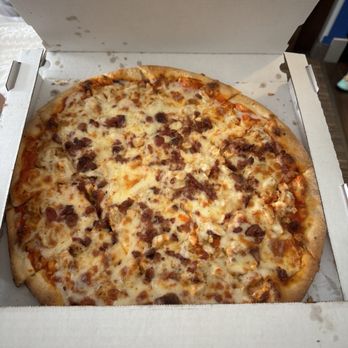 Juanito’s Pizza - bacon chicken buffalo ranch - A pizza with a golden crust topped with melted cheese, bacon bits, chicken pieces, and drizzled with buffalo sauce and ranch dressing, inside an open white pizza box. The box is on a surface with part of a wall and some furniture visible in the background. - Pizza Near Me - Beloit, Wisconsin
