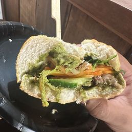 Banh Mi - A sandwich filled with vegetables and avocado, served on white bread, held in a person's hand over a black plate.