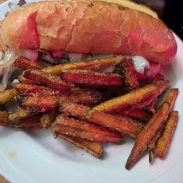 Cajun Steak Sandwich - A plate features a prime rib steak sandwich with a toasted bun and seasoned sweet potato fries, served on a white dish.