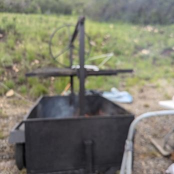 Katy Q's BBQ - A black barbecue grill with a wheel and handle is set outdoors on grass, with a blurred background of greenery and a hill. - Caterers Near Me - Delta, Colorado