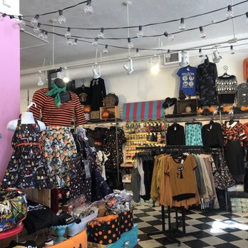 Sidecca - Inside of the shop - The image shows the interior of a vintage clothing store featuring a variety of women's apparel and accessories. Mannequins display dresses and tops with retro patterns, and racks hold additional clothing items in different colors and styles. The store has decorative elements like string lights, Halloween-themed decorations, and a checkered black-and-white floor. Shelves and tables are filled with accessories, bags, and small decorative items, creating a colorful and eclectic shopping environment. - Accessories Near Me - Altadena, California