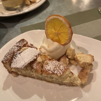 Terre - Vanilla gelato and cake - A slice of apple pie with powdered sugar, served with whipped cream topped with a lemon slice, on a white plate. - Italian Near Me - Brooklyn, New York