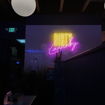 Dirty Laundry - Inside - Neon sign with 'DIRTY Laundry' in yellow and pink lights is mounted on a dark brick wall inside a bar or lounge. - Cocktail Bars Near Me - Denver, Colorado