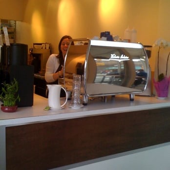 Milano Coffee Roasters - Kelly peeks out from behind the sleek espresso machine. - Coffee & Tea Near Me - Vancouver, British Columbia Milano Coffee Roasters - Kelly peeks out from behind the sleek espresso machine. - Coffee & Tea Near Me - Vancouver, British Columbia