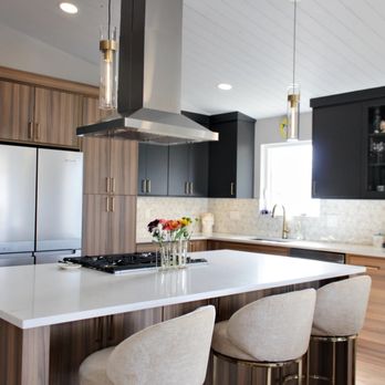 HOMEfix - Modern kitchen with walnut and black cabinets, a large white island with beige stools, stainless steel refrigerator, and pendant lights. - General Contractors Near Me - Colorado Springs, Colorado HOMEfix - Modern kitchen with walnut and black cabinets, a large white island with beige stools, stainless steel refrigerator, and pendant lights. - General Contractors Near Me - Colorado Springs, Colorado