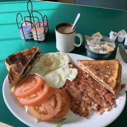 Cornbeef hash with eggs over easy and tomato slices instead of country potatoes or hash browns and sourdough toast and cup of coffee.