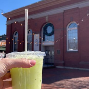 The Freshmobile - a hand holding a drink in front of a brick building - Juice Bars & Smoothies Near Me