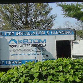 Keltom Gutter Services - A large service truck with Keltom Gutter Services branding is parked on a grassy area, with trees and bushes in the background. The truck features signage for gutter installation, cleaning, and repair, along with contact information and a website. The scene suggests outdoor gutter maintenance work in a suburban or rural setting. - Gutter Services Near Me - Berkeley Heights, New Jersey